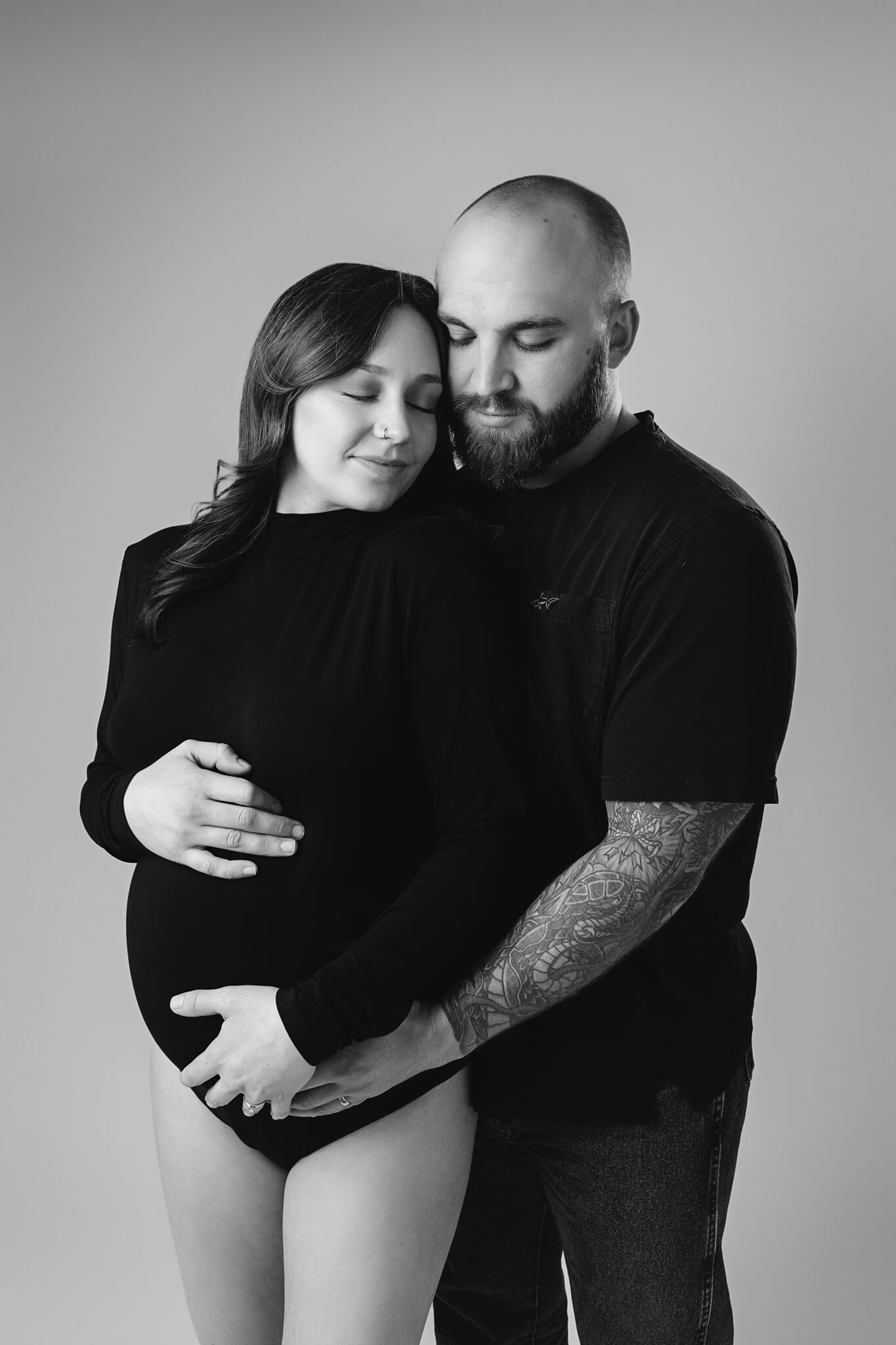 A mother to be leans into her husband while standing in a studio holding the bump in a black one piece after meeting with austin birth centers