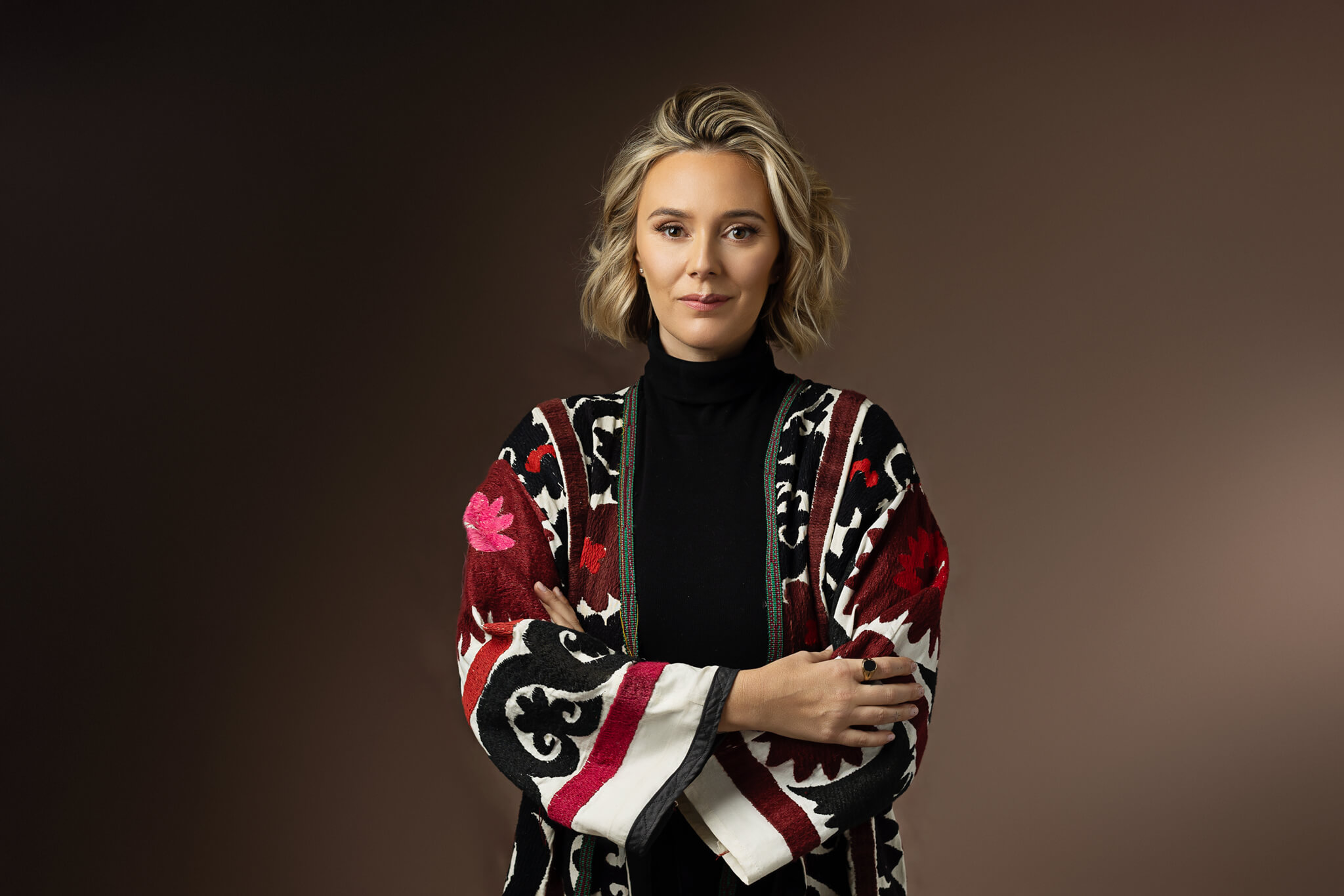 A woman with short blonde hair stands in a studio in a designer jacket smiling with arms crossed after visiting austin hair salons