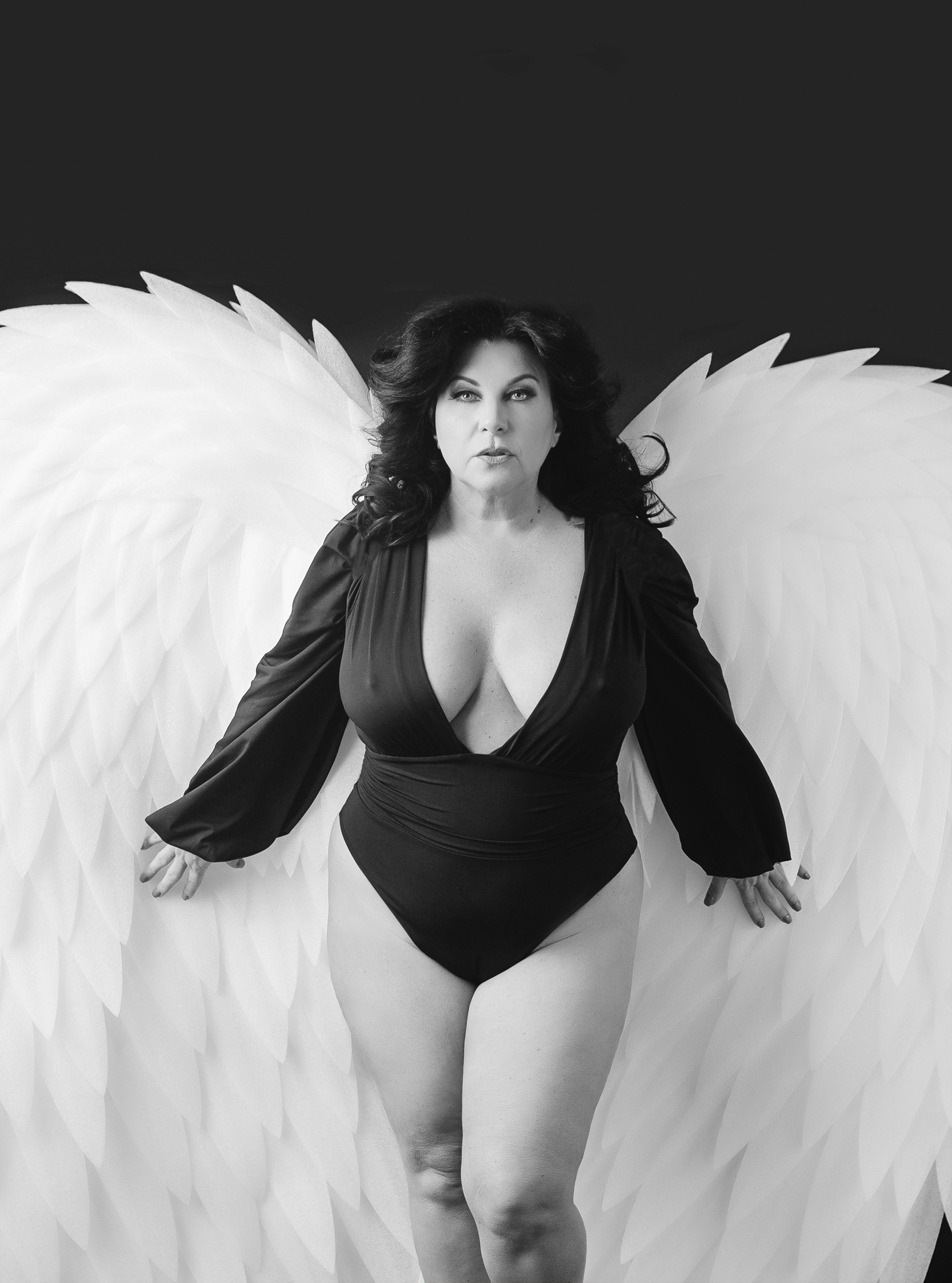 A woman in a black onesie stands in a studio with large white wings after austin brazilian wax