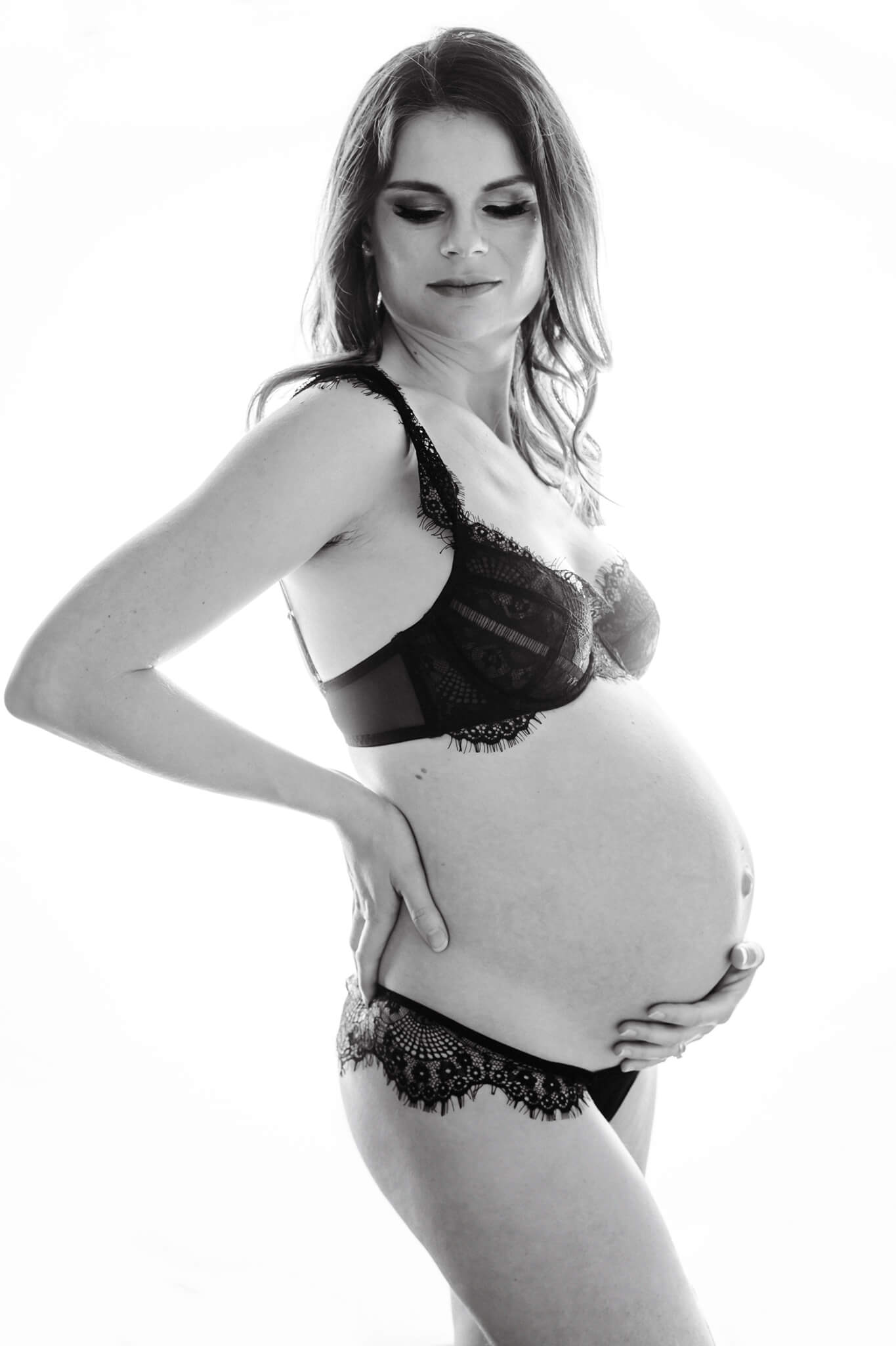 A mother to be stands in a studio holding her bump in lace lingerie