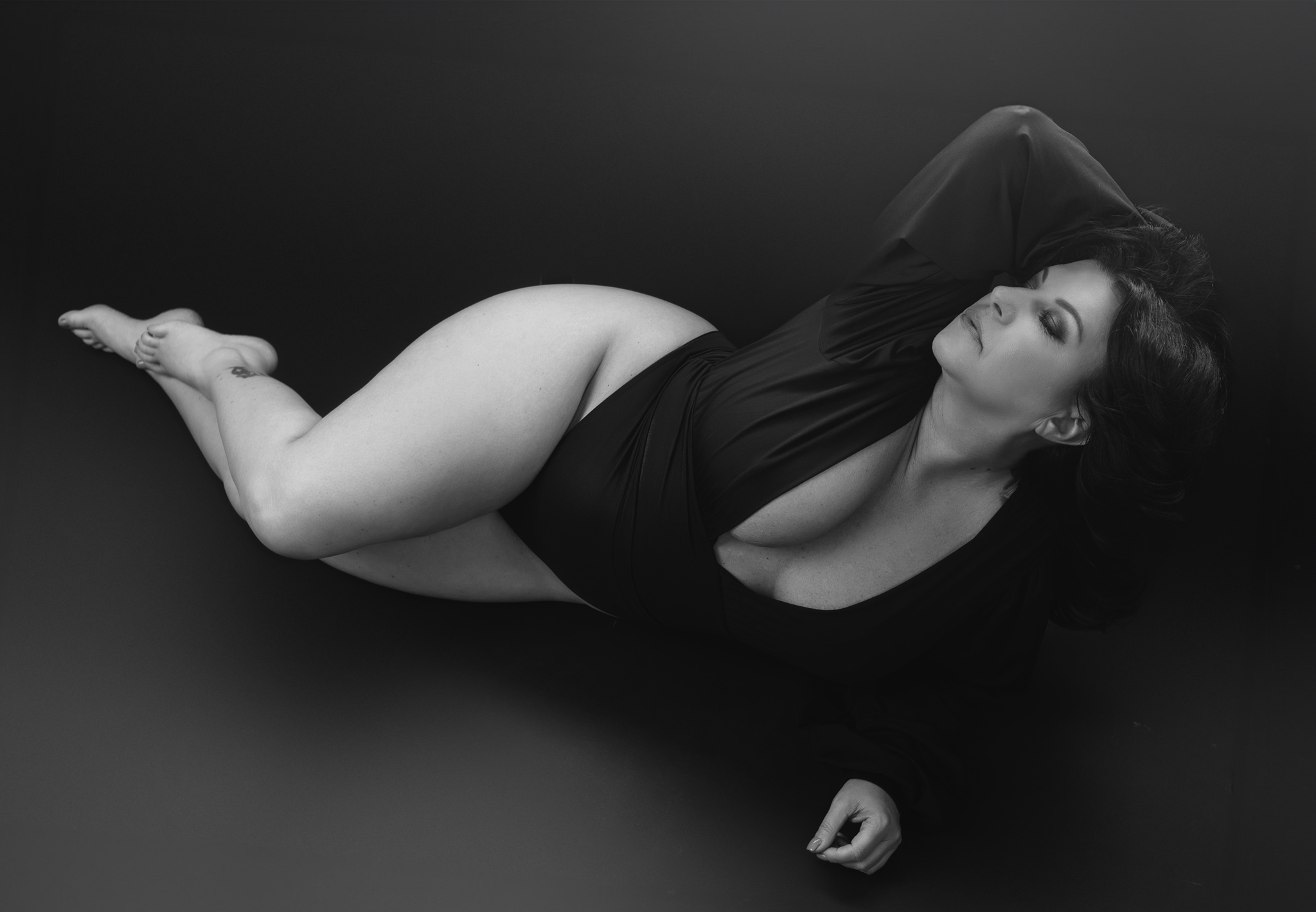 A woman in a black one piece lays across a studio floor with her hand in her hair after some austin hot yoga