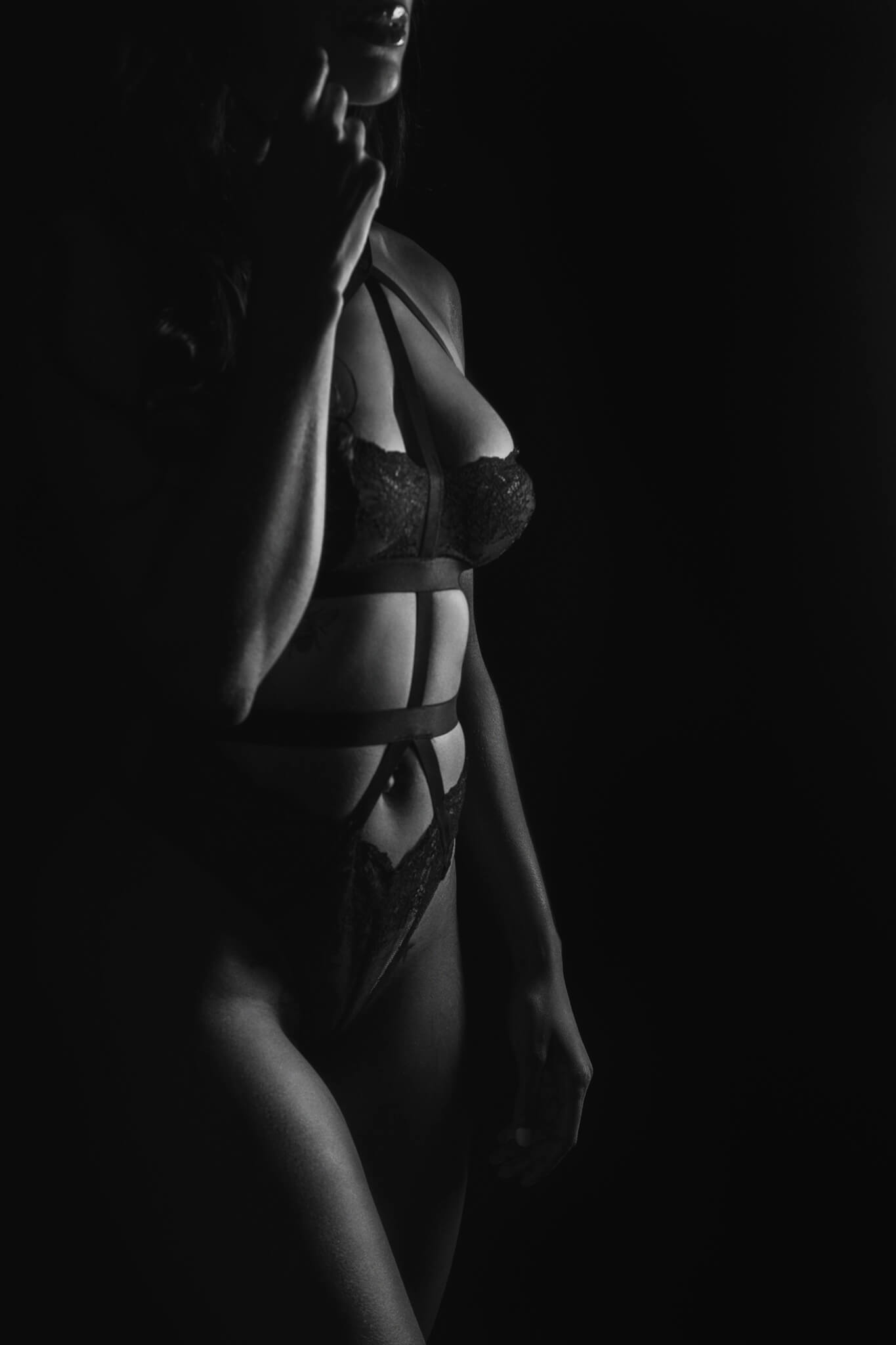 A dark image of a women in lace and strap lingerie walking in a studio