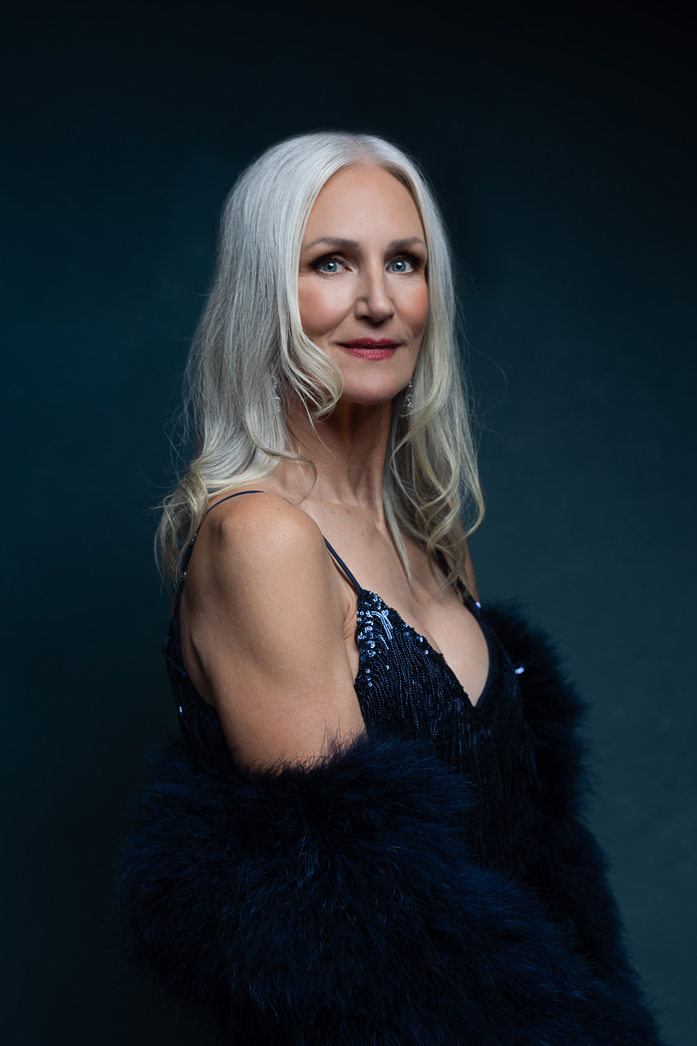A woman in blue fur and sequence stands in a studio smiling before visiting romantic restaurants in austin