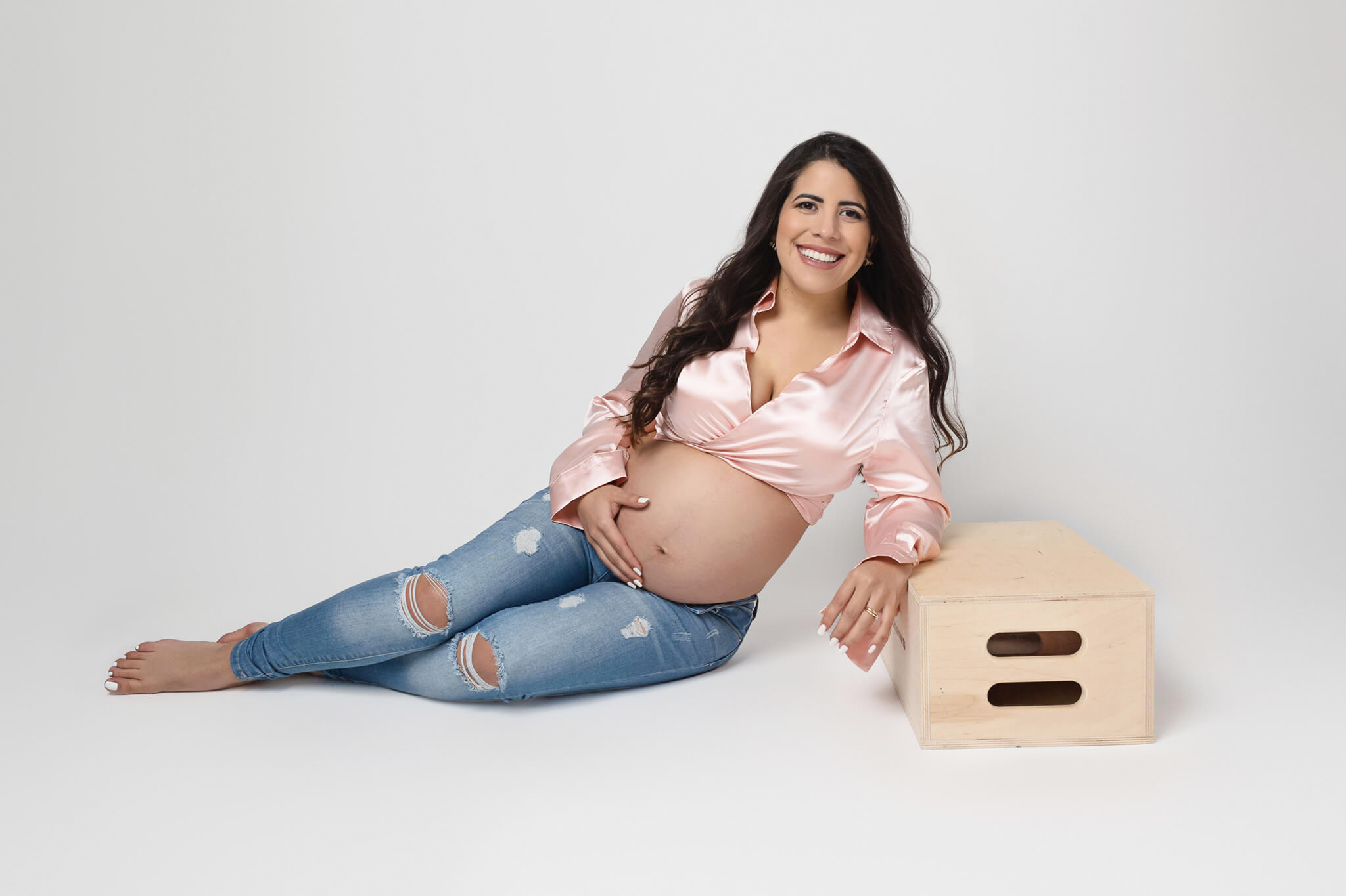 pregnant woman is posing wearing a pink top and jeans in her maternity photography session