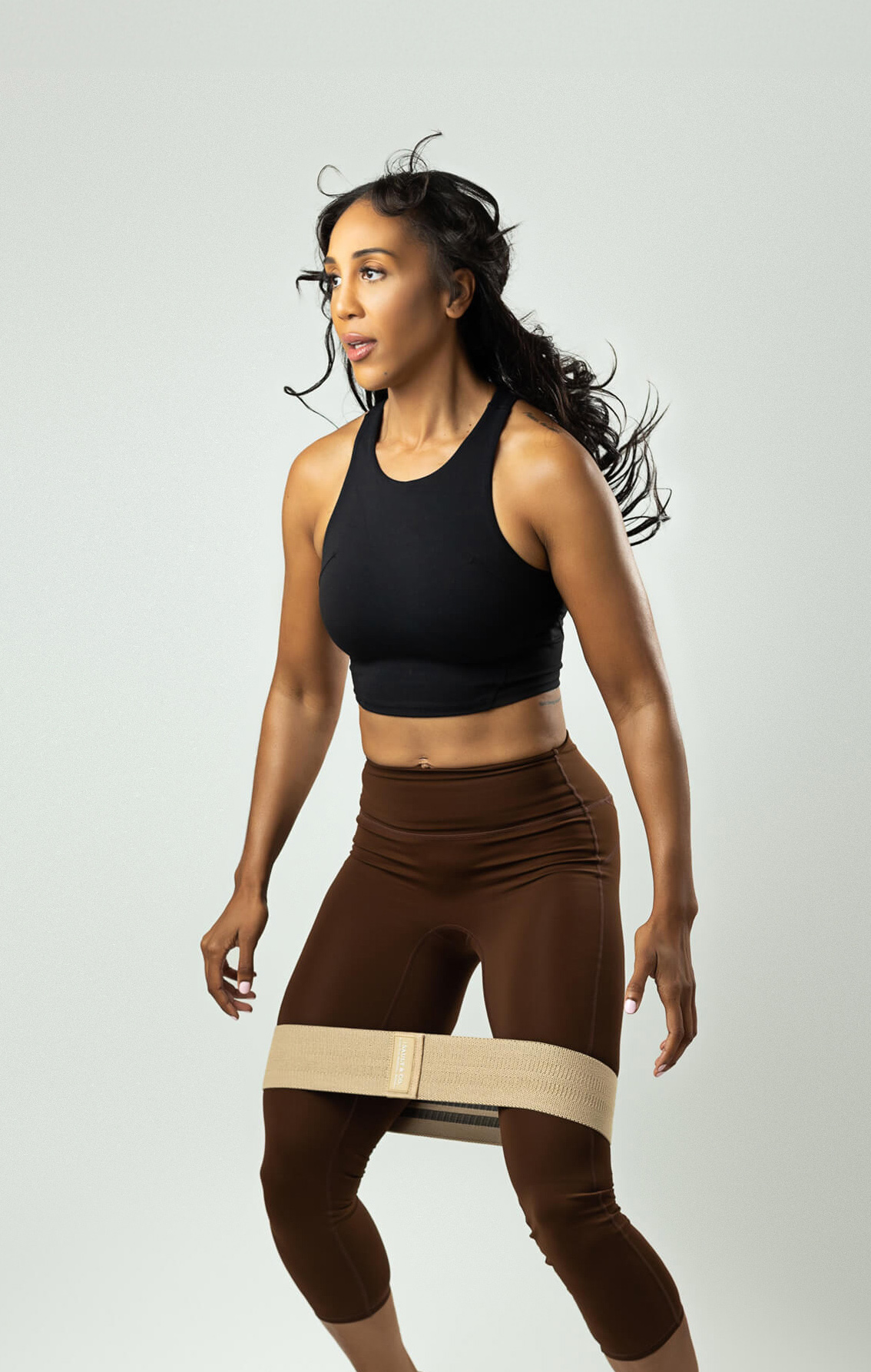 Fitness model is posing while showing her athletic clothing brand over white backdrop in a studio branding photoshoot