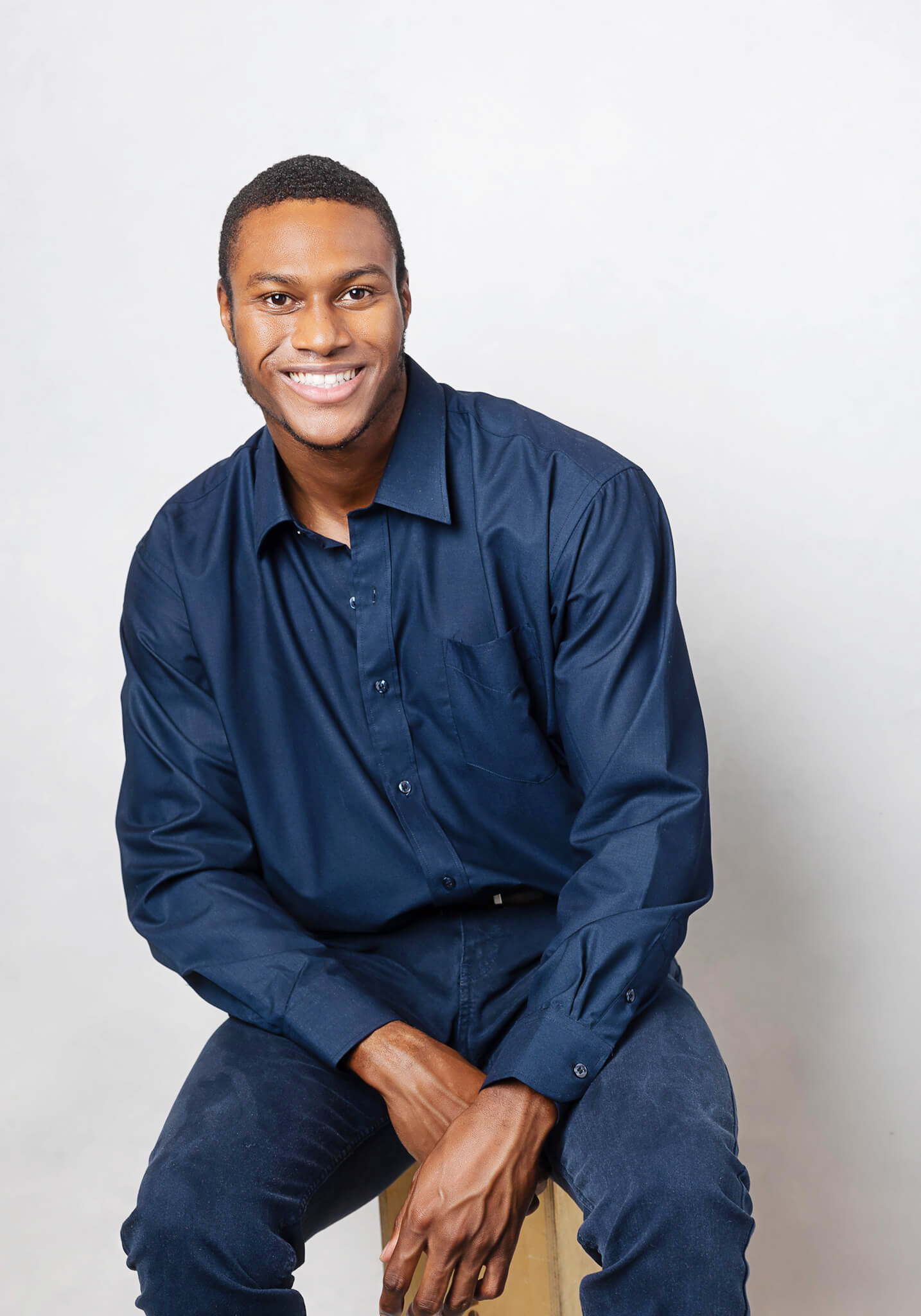 Young actor is sitting and posing with a relaxed face and smile wearing jeans and a blue shirt