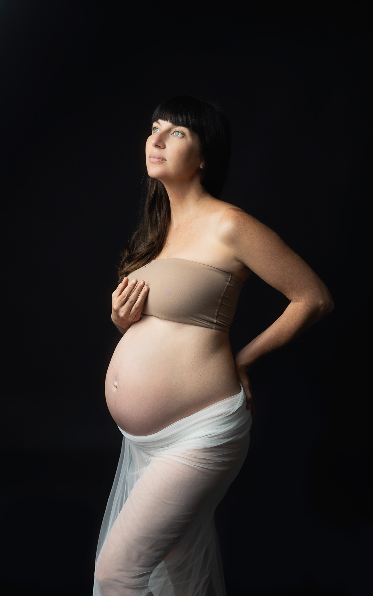 maternity session in Austin Texas of a woman looking up to the light and black backdrop 