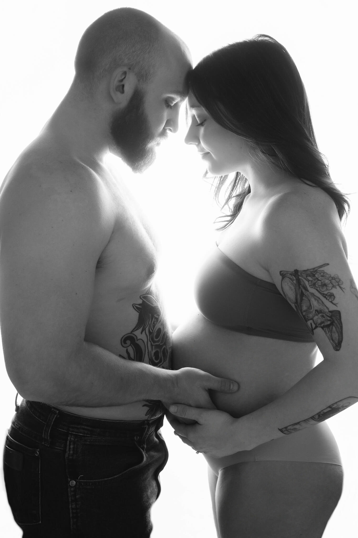 couple pose for a maternity session on a white high key backdrop for a black and white image showing a strong connection