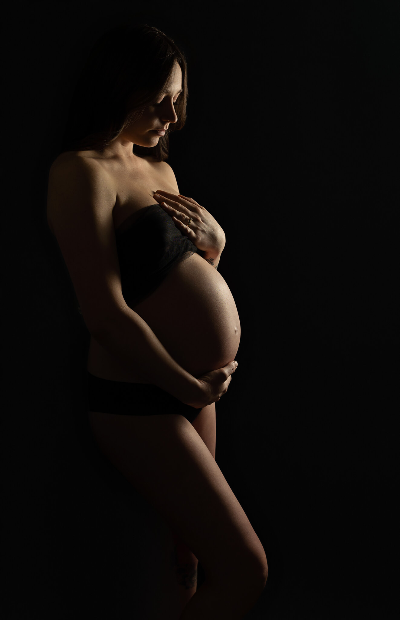 beautiful and artistic maternity studio picture of a young woman wearing black tulle touching her belly