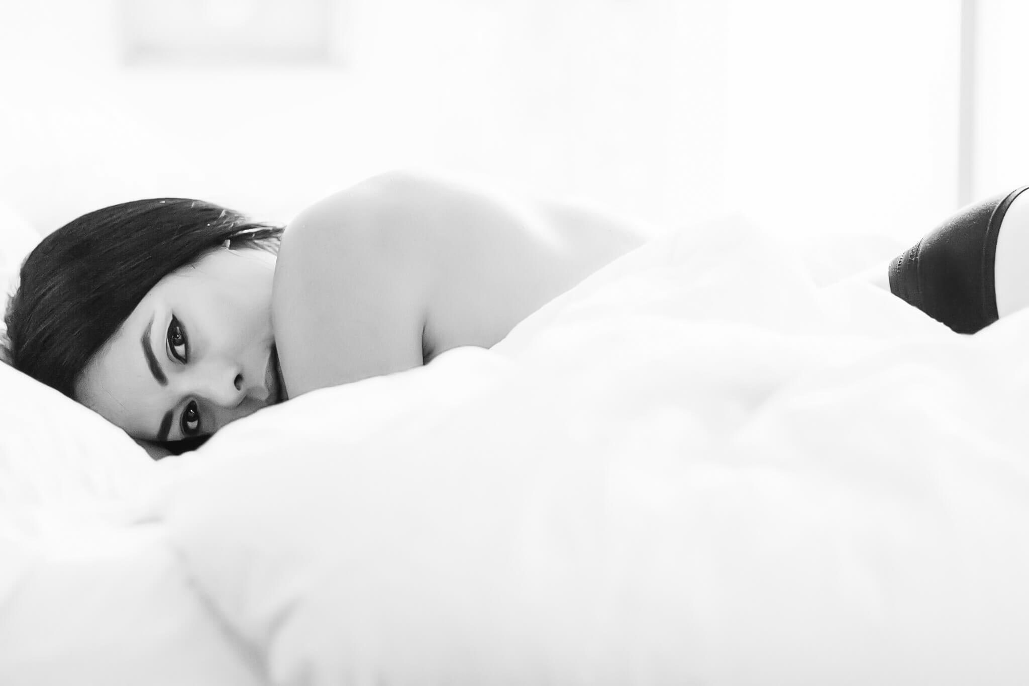 very intimate image on a bed full of white sheets, this woman is looking at the camera and is semi nude for this boudoir session in Austin, TX