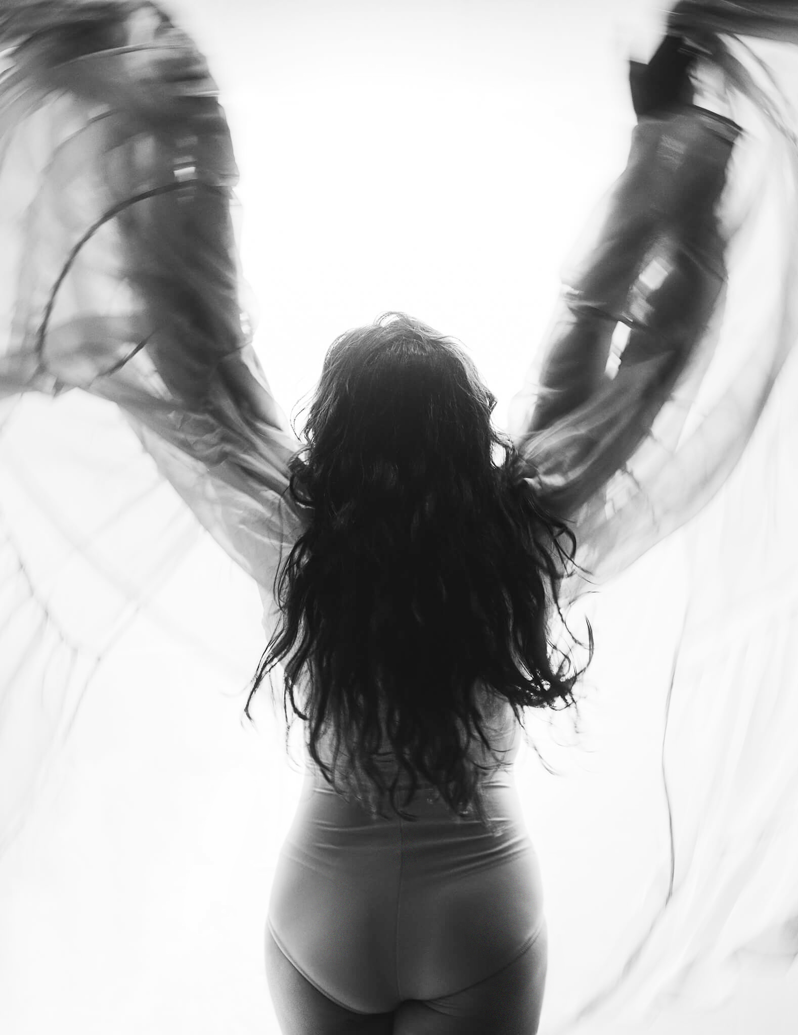 artistic anonymous image of a woman waving a big piece of fabric in a backlit setup