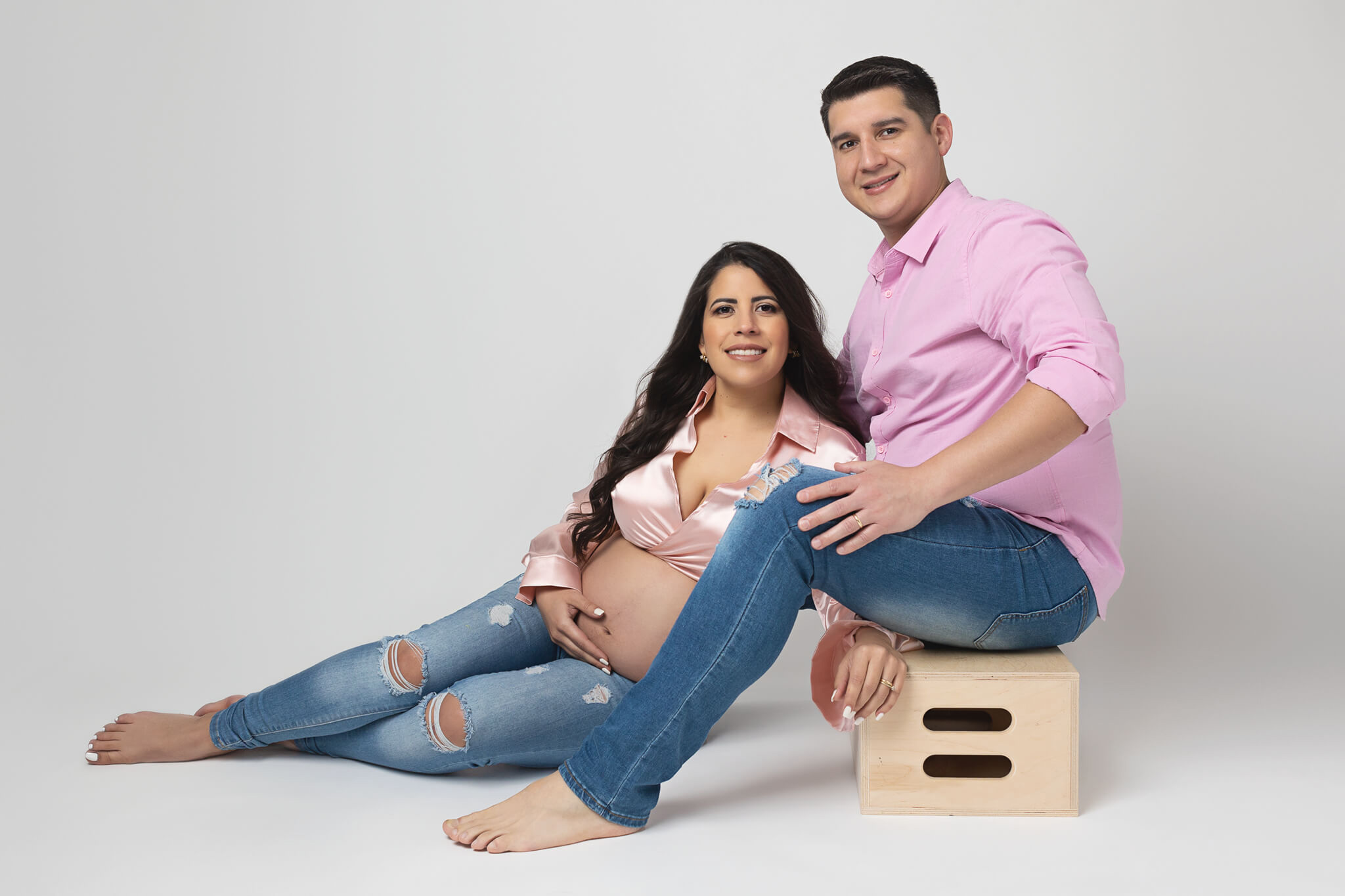 expecting couple wearing pink over white backdrop smiling at the camera