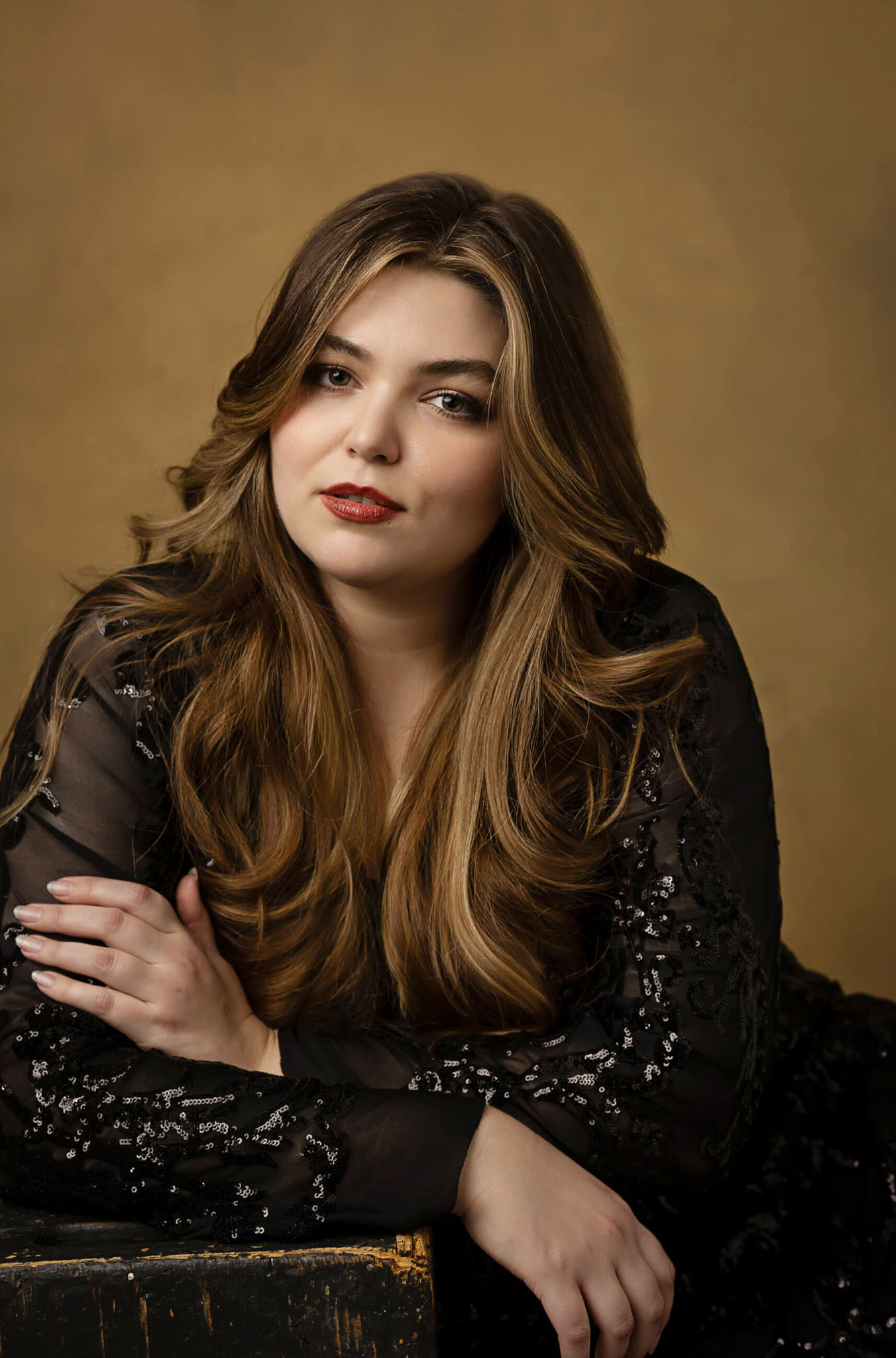 studio image of a young lady wearing a black dress with a brown backdrop for her senior indoor photoshoot