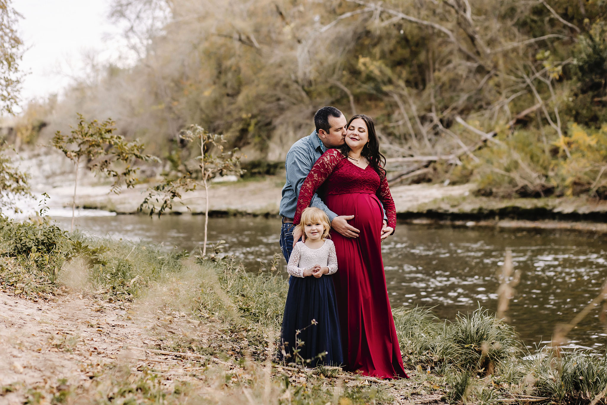 family and maternity session at a creek where you can see their connection and the beautiful red gown she is wearing